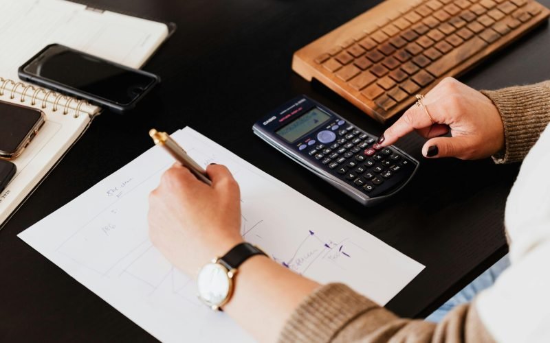 Close-up of hands working with a calculator and notebook on a desk, analyzing documents.