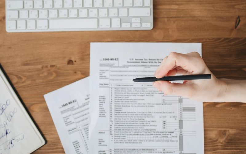 Close-up of a hand holding a pen over US tax forms on a wooden table.