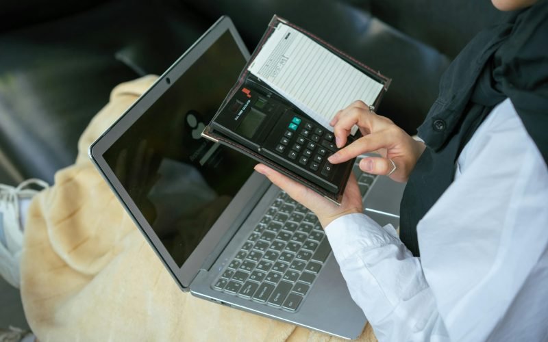 Close-up of a person using a calculator with a laptop, symbolizing home office productivity.